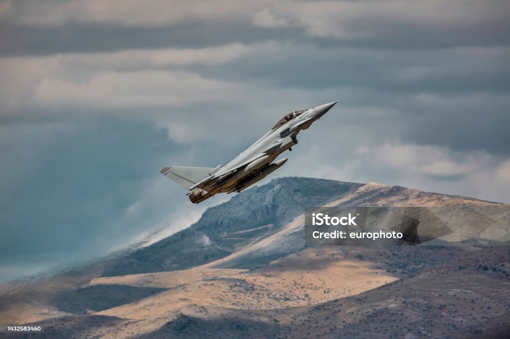 5th generation military jet fighter flying an Eurofighter Typhoon airplane climbing up towards sky in front of a hill Transportation Stock Photo