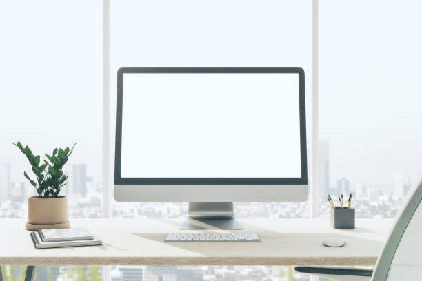 istock Front view on blank white modern computer monitor on light wooden table with flower pot, keyboard and notebooks in sunny office with city view from window. 3D rendering, mockup 1432586651