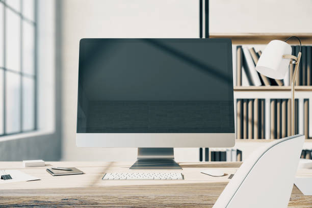 istock Front view on blank modern computer monitor with copyspace for your text or logo on wooden table with white keyboard and stylish lamp in sunny office with bookcase on background. 3D rendering, mockup 1432586691