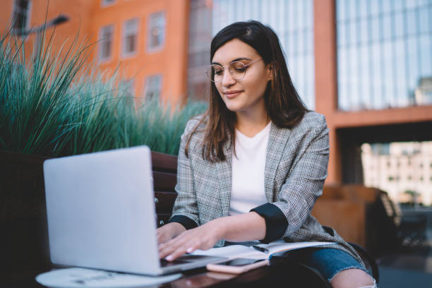 istock Smart caucasian female freelancer typing on laptop computer wear spectacles for vision protection having remote job outdoors, positive student prepare homework making research browse web page 1432587858