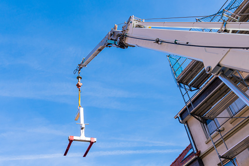 Construction crane boom with a load feeder against the backdrop of a house under construction.