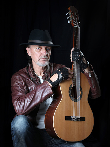 A man in a hat and with a guitar on a black background. Self portrait.