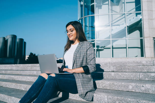 istock Young prosperous female freelancer using laptop computer for remote job browse web pages and keyboarding on urban settings, positive woman student enjoying sunny weather and watching webinar 1432589428