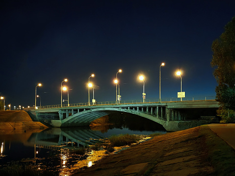 On the arched bridge over the river at night, a row of street lamps with bright lamps against the background of the sky
