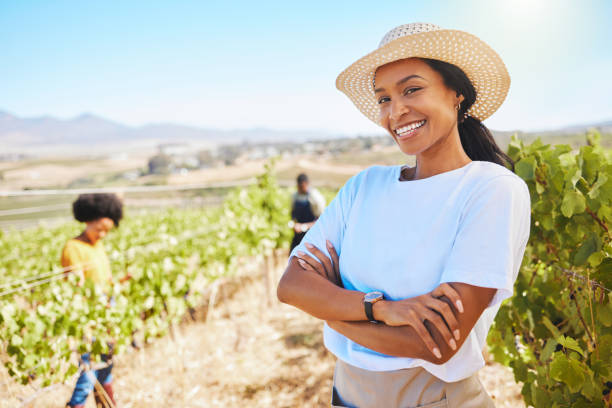 selbstbewusster oder stolzer bauer mit verschränkten armen und lächelndem weinberg landwirtschaftliches feld. junge frau auf nachhaltigem wein- oder grünem obsthof im sommer. arbeitnehmer zufrieden mit der nachhaltigkeit des wachstums auf dem land - bäuerin stock-fotos und bilder