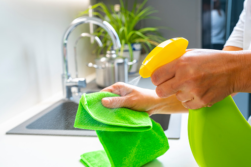 Cleaning concepts: Close up view of woman's hands cleaning kitchen counter surface with a microfiber rag and soap in a spray bottle High resolution 42Mp indoors digital capture taken with SONY A7rII and Zeiss Batis 40mm F2.0 CF lens