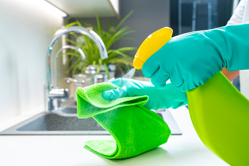 Cleaning concepts: Close up view of hands with washing up gloves cleaning kitchen counter surface with a microfiber rag and soap in a spray bottle High resolution 42Mp indoors digital capture taken with SONY A7rII and Zeiss Batis 40mm F2.0 CF lens