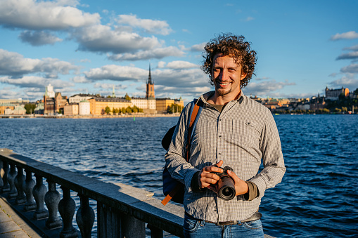 Portrait of a handsome young man holding a camera on the quayside in Stockholm, Sweden.