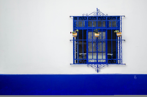 An ornate window painted blue against a vibrant white and blue wall in Lima, Peru