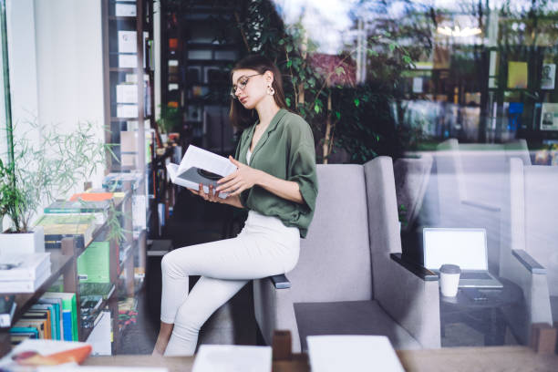 istock Pretty young female reading book in library 1432593338