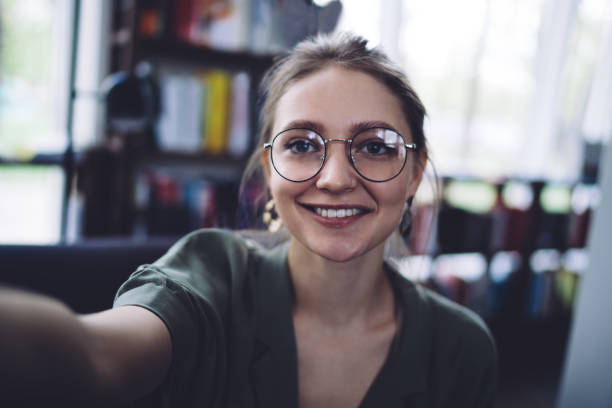 istock Smart student with wide smile taking selfie in library 1432593382