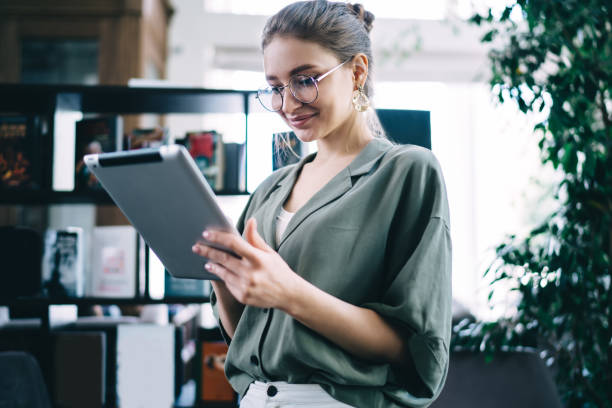 istock Concentrated woman standing with tablet in library 1432593386