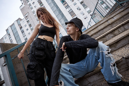 A teenage couple is posing outside on the stairs surrounded by buildings.