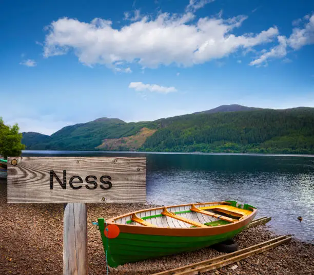 Loch Ness with wooden sign photomount and beached boats in Scotland Highlands UK famous for the Nessie monster sightings.