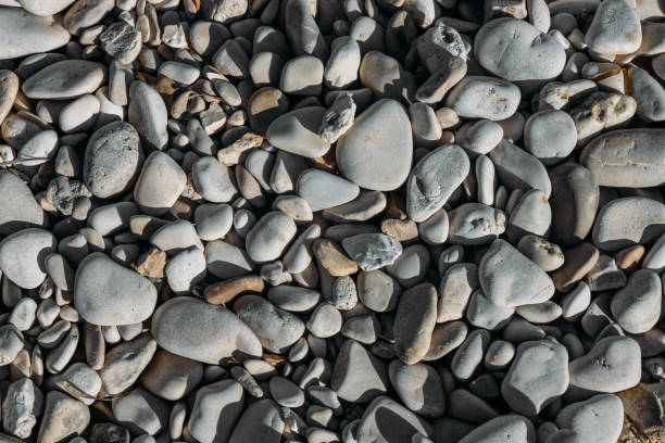 Smoothed, rounded pebbles washed up on a storm ridge of a beach at Ballyquintin Point County Down, Northern Ireland.  In the distance, out of focus, is a sandy beach, the water's edge and the lower half of a person's body.