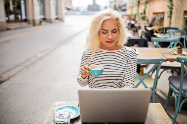 istock Mature woman outdoors drinking coffee using laptop 1432601666