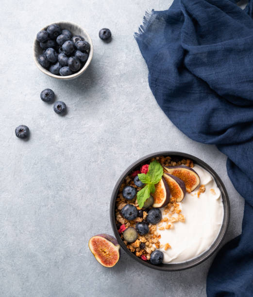 Natural yogurt with muesli, berries and figs in a black bowl on a blue background with napkin. Healthy and nutritious breakfast.