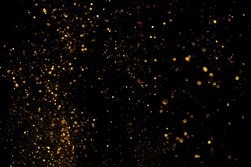 Golden glitter shiny dust particles glowing lights bokeh dark abstract background