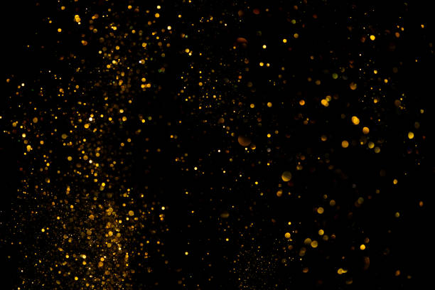 Golden glitter shiny dust particles glowing lights bokeh dark background stock photo