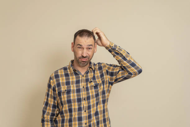 istock Doubtful bearded hispanic man in a plaid shirt thinking, scratching his head trying to find a solution, isolated on a beige background 1432603848