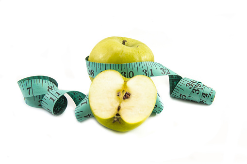 Measuring tape wrapped around a green apple as a symbol of diet.