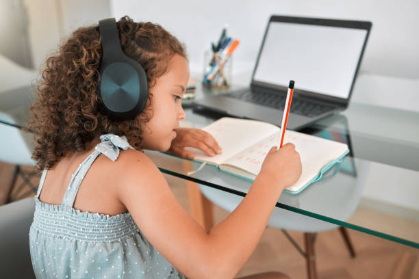 istock Homeschooling by a smart and clever little girl attending online or virtual class using a laptop and headphones. A young child writing and working or doing homework at home listening to music 1432610966