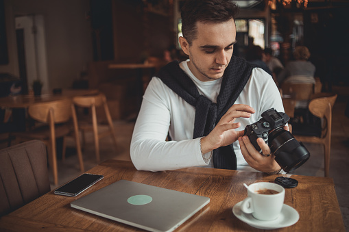 A young freelance photographer sits in a cafe and works, taking photos that he uses for work