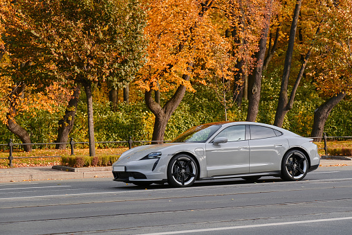 Sankt-Peterburg, RUSSIA - 12 october 2022 : Porsche Taycan Turbo S driving on the road. Expensive sports car on the background of autumn foliage.
