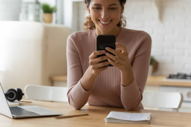 istock Close up smiling woman using smartphone, sitting at wooden table 1432616203