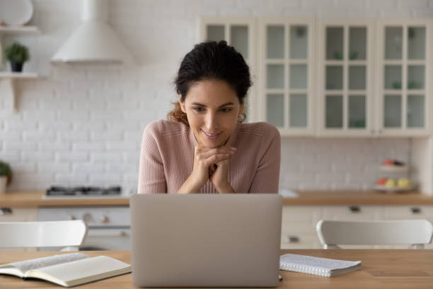 istock Smiling woman looking at laptop screen, working online in kitchen 1432616207