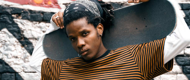 retrato de un joven apuesto y elegante hombre negro con rastas afro de cabello natural. chico afroamericano. escaleras, pared pintada con graffiti en el barrio pobre del distrito de la ciudad de la cultura del arte callejero. hombre skater afroamericano. m - graffiti men wall street art fotografías e imágenes de stock