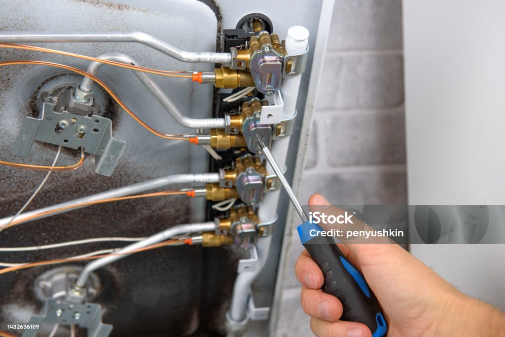 Handyman repairs or maintains a gas stove with a screwdriver Disassembling Stock Photo