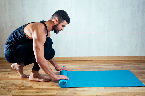 The man's hand spreads the yoga mat on the floor. blue yoga mat.