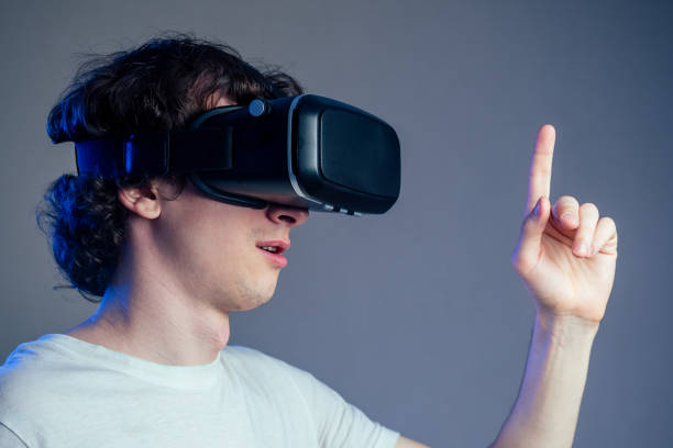 istock portrait of a young man in virtual reality points points his finger gray wall background. The concept of games in the mask of virtual reality 1432637071