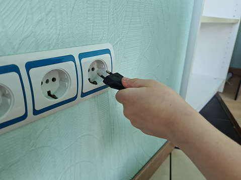 Child holding hand and inserting plug into outlet. Power line with switches and sockets and child concept