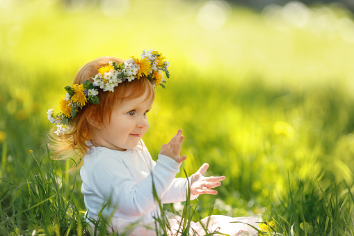 Cute little girl is wearing beautiful spring wreath outdoors, space for text. Red hair baby is spending time on nature