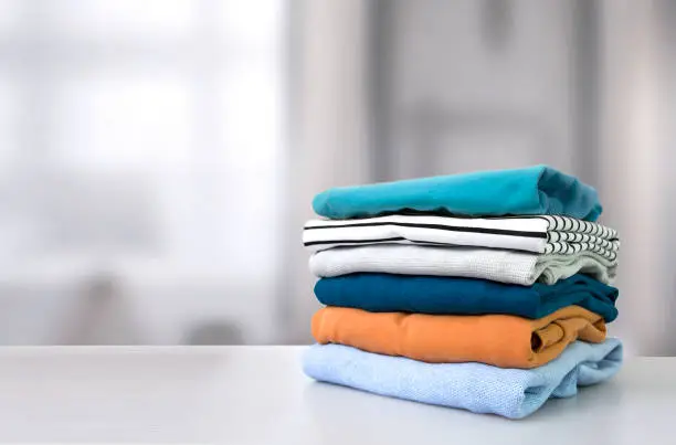 Photo of Stack of colorful clothes. Pile of clothing on table empty space background.