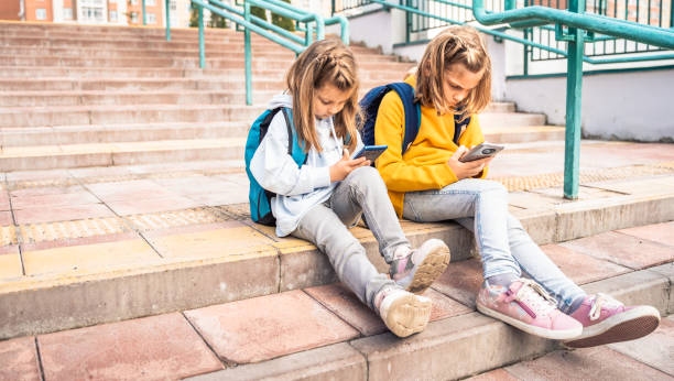 istock Back to elementary,primary school. Little girls with backpack,mobile phone.Chat, talk with mom,friends, classmates on break.Autumn study after vacation. Education of children.Pupil kid on stair steps 1432642870