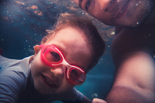 Child girl swimming with father underwater