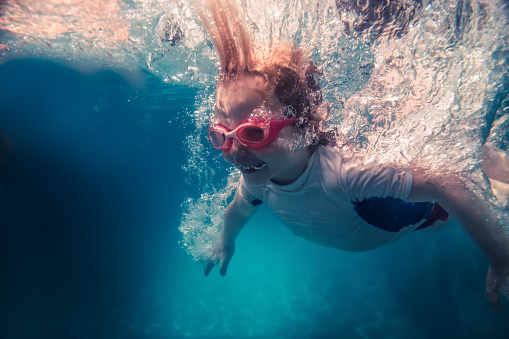 Child girl jumping into water with splashes and swimming underwater