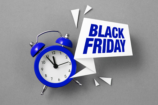 Blue alarm clock with colored papers and Black Friday text on gray background