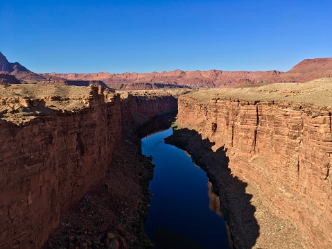 The Marble Canyon landscape surrounds the Colorado River. With the blue sky being reflected in the river below.