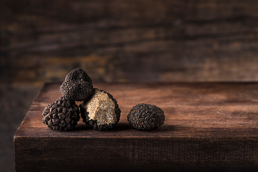 Black truffles in antique  wooden board, rustic style, low key, selective focus, macro, copy space for text. Season of black truffle. Autumn gourmet cuisine of Piedmont, Northern Italy, Spain and France