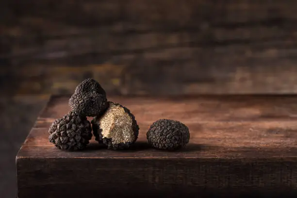 Black truffles in antique  wooden board, rustic style, low key, selective focus, macro, copy space for text. Season of black truffle. Autumn gourmet cuisine of Piedmont, Northern Italy, Spain and France