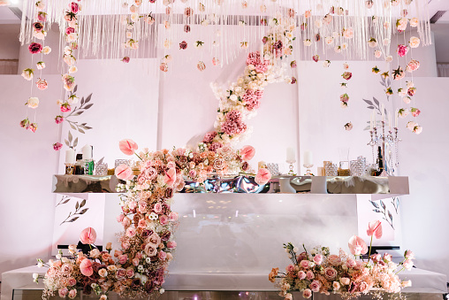 Festive table, arch, stand, garland decorated with a composition of pink flowers and greenery, candles in the banquet hall. Table newlyweds in the banquet area at the wedding party.