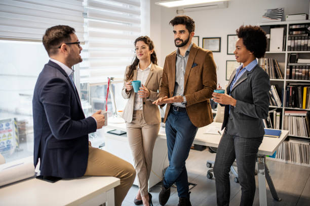 istock Group of smiling colleagues standing at workplace, chatting and drinking coffee on pause 1432655677