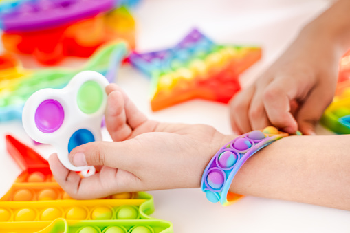 Little girl,kid,child plays with colorful pop it bracelet.Children's room.Funny trendy silicone antistress colorful sensory push toy popit.Flapping fidget.Rainbow color.Cure of autism.Stress reliever.