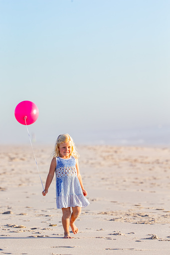 Little girl enjoying a day on the beach with her pinky balloon