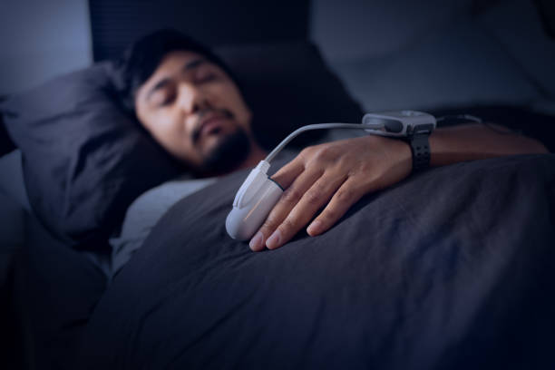 Man Wearing a Pulse Oximeter - At Home Sleep Study Test for Sleep Apnea Asian Man Wearing a Pulse Oximeter in Bed - At Home Sleep Study Test for Sleep Apnea - Blood Oxygen Saturation Monitor - Sleep Hypoxia - Disrupted REM Sleep - Daytime Sleepiness and Fatigue 
Shot with Canon R5 pulse oxymeter stock pictures, royalty-free photos & images