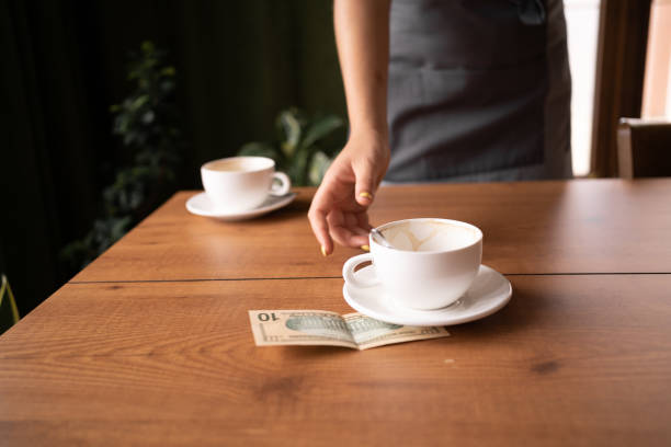 femme prenant une tasse avec des billets de banque en dollars américains sur la table du café, deux tasses de thé sur le fond. paiement, frais de service, vérification des factures, pourboires d’argent. - wallaroo photos et images de collection